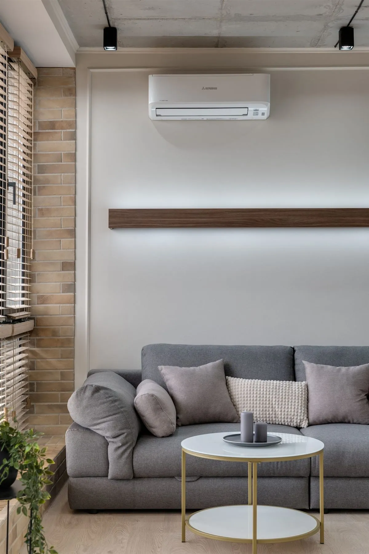 Jasny salon z szarą sofą, drewnianymi detalami i klimatyzatorem ściennym